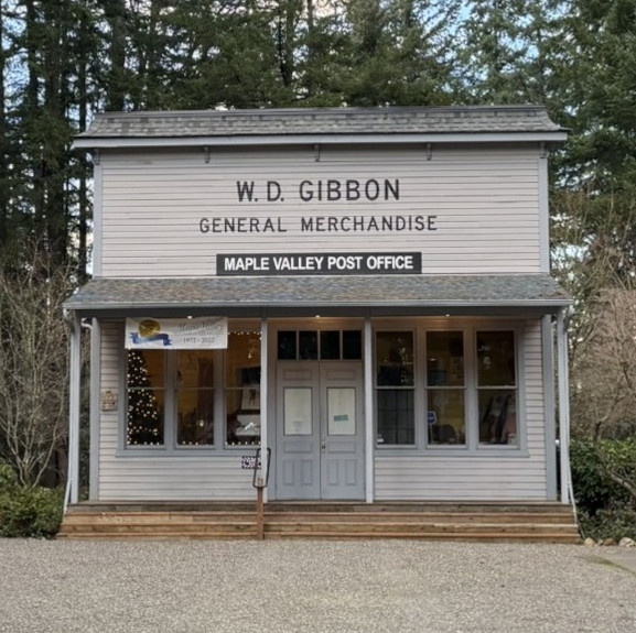 Gray building with the words "W.D. Gibbon General Merchandise" and "Maple Valley Post Office" painted above the entryway.