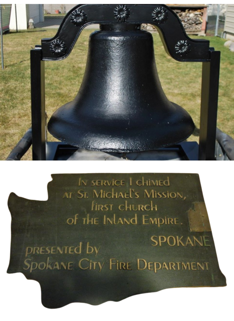 Bell painted black outside in front of a grassy lawn. Below, a plaque shaped like Washington State that reads, "In service I chimed at St. Michael's Mission, first Church of the Inland Empire. Spokane. Presented by Spokane City Fire Department."